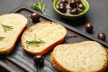 Wooden board with slices of fresh bread and olives on dark background, closeupの写真素材