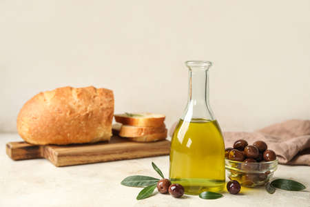 Bottle of fresh oil and bowl with olives on light background