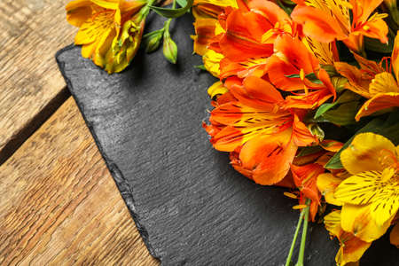 Slate board with beautiful alstroemeria flowers on wooden background, closeupの写真素材