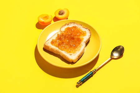 Plate of delicious toast with apricot jam on yellow background