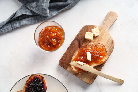 Wooden board of toast with jam and butter on light background