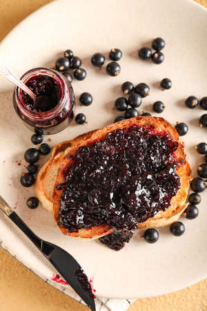 Plate with tasty toast, black currant, jar and knife on beige background, closeupの写真素材