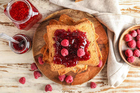 Plate with tasty toasts and raspberry jam on white wooden background