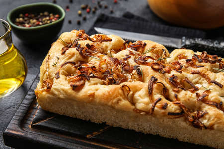 Wooden board with tasty Italian focaccia on dark table, closeup