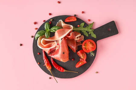Slate board with delicious jamon, spices and tomatoes on pink backgroundの写真素材