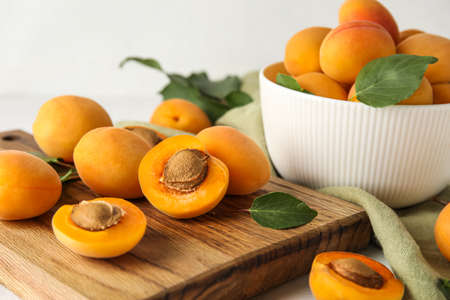 Wooden board with ripe apricots on light background, closeup
