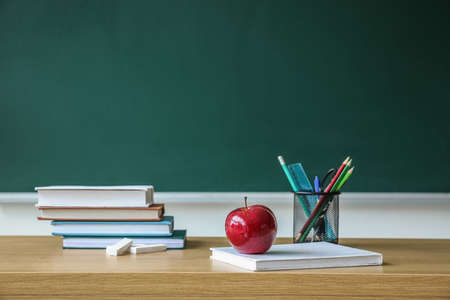 Apple with school books and pen cup on table near chalkboardの写真素材