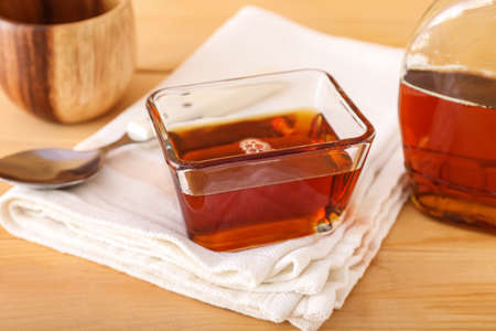 Glass bowl of maple syrup on wooden table, closeup