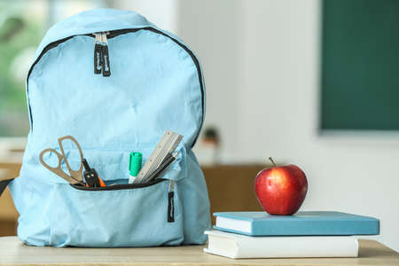Apple with school books and backpack on table in classroom