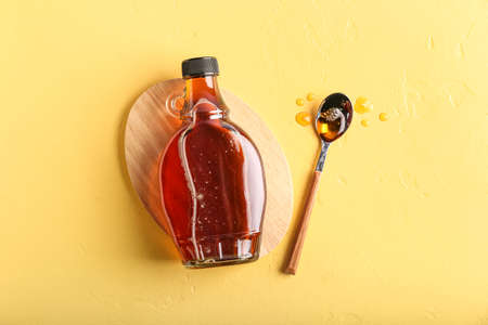Bottle and spoon of maple syrup on color backgroundの写真素材