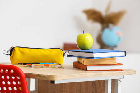 Apple with school books and pencil case on table in classroomの写真素材