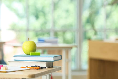 Apple with school books and stationery supplies on table in classroomの写真素材