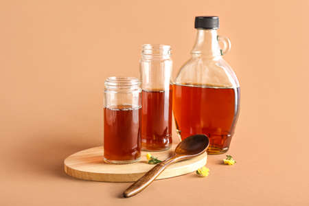 Wooden board with jars and bottle of tasty maple syrup on color background
