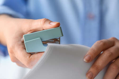 Woman with blue stapler and paper sheets at table, closeupの写真素材