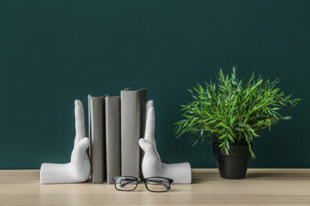 Stylish holder with books, eyeglasses and houseplant on table near green wallの写真素材