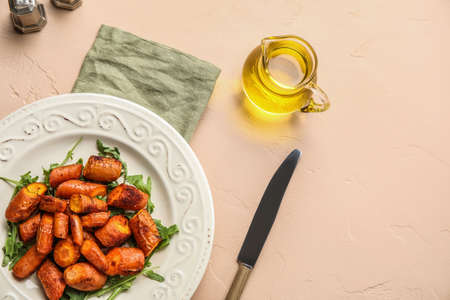 Plate with tasty baked carrots and pitcher of oil on color backgroundの写真素材