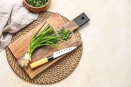 Wooden board with bunch of green onion and knife on light backgroundの写真素材