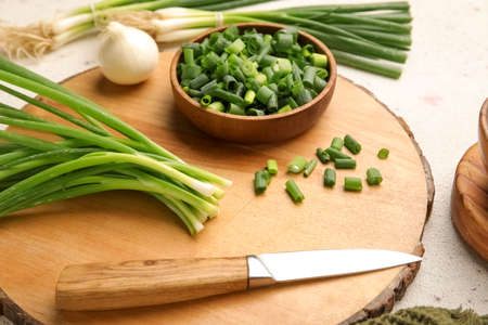 Wooden board with bunch of green onion and knife on table, closeupの写真素材