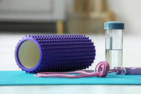 Foam roller with skipping rope and bottle of water on mat in living room