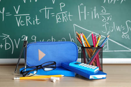 Pencil case with school stationery and eyeglasses on table near chalkboard