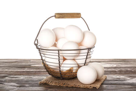 Basket with chicken eggs on wooden table against white background