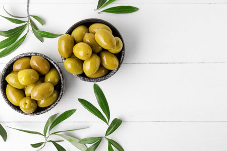 Composition with bowls of tasty green olives and leaves on light wooden backgroundの写真素材