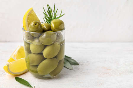 Glass with tasty green olives and lemon slice on table