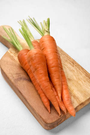 Wooden board with fresh carrots on light background, closeup