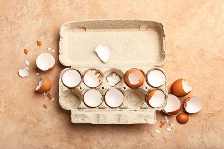 Cardboard holder with broken egg shells on color background