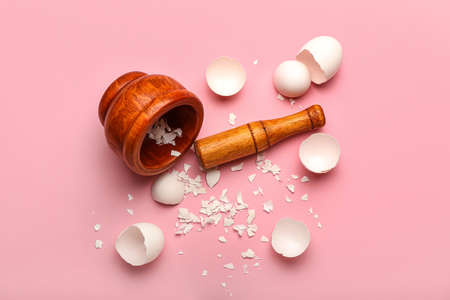Wooden mortar and pestle with broken egg shells on pink backgroundの写真素材