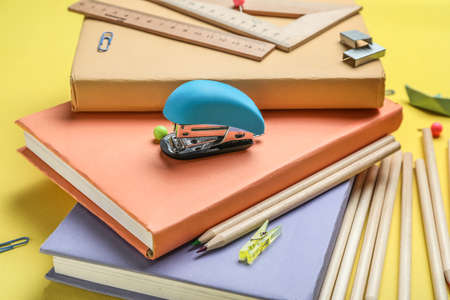 Stapler with different stationery supplies on yellow background