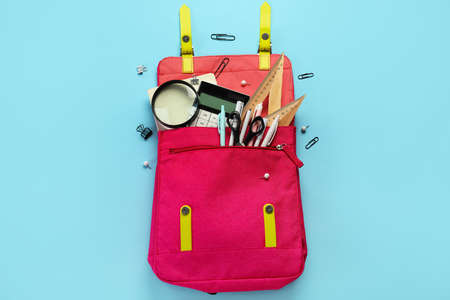Pink backpack with school stationery on blue background