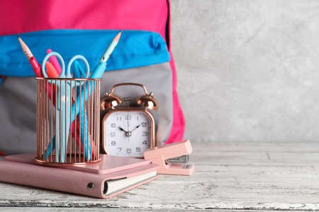 Pen cup with school stationery, alarm clock and backpack on table against grunge backgroundの写真素材