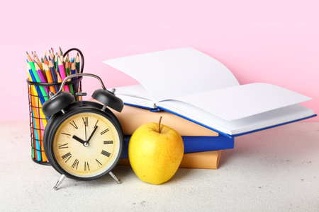 School stationery with apple and alarm clock on table against pink backgroundの写真素材
