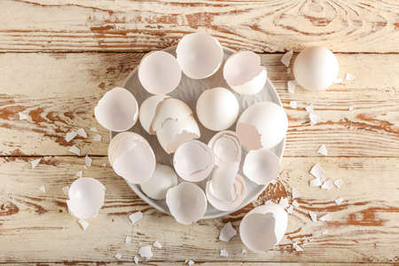 Plate with broken egg shells on light wooden background