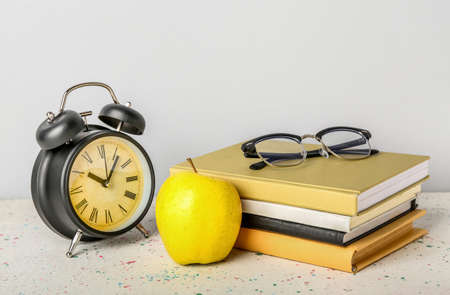 School books with apple, eyeglasses and alarm clock on table against gray backgroundの写真素材