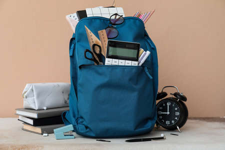 School backpack with stationery and alarm clock on table against beige backgroundの写真素材