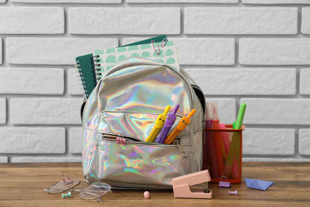 School backpack with stationery on table against white brick background