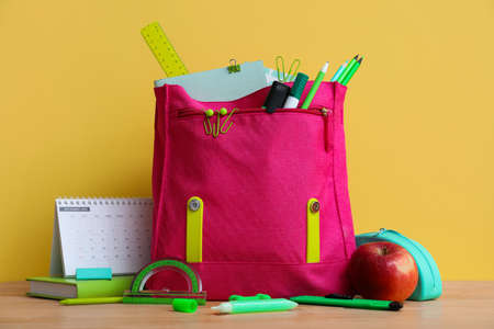School backpack with stationery, apple and calendar on table against yellow backgroundの写真素材