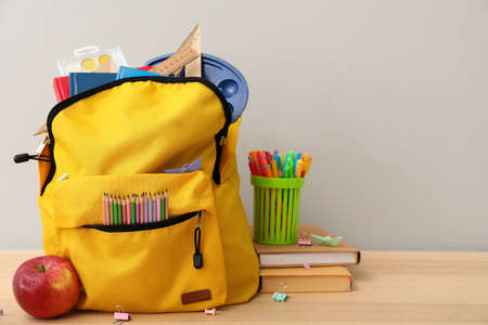 School backpack with stationery and apple on table against gray backgroundの写真素材