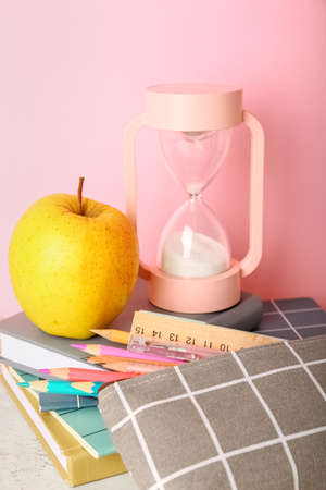 School stationery with apple and hourglass on table against pink backgroundの写真素材
