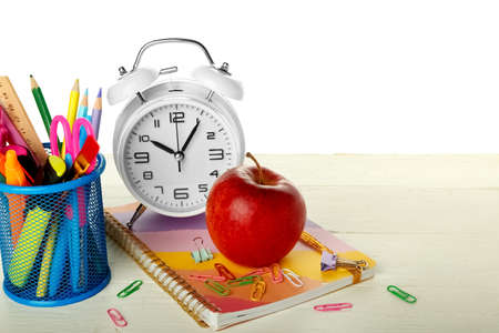 School stationery with apple and alarm clock on table against white backgroundの写真素材