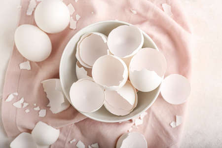 Bowl with broken egg shells and napkin on white background
