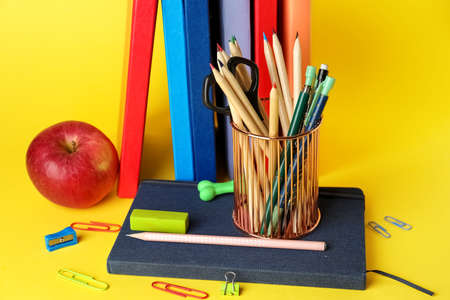 Pen cup with school stationery, apple and books on yellow background