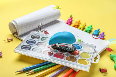 Stapler with paints and stationery supplies on yellow background, closeup