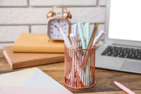 Metal cup with pens and pencils on table near white brick wall, closeupの写真素材