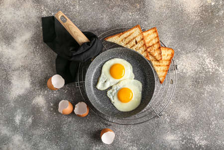 Frying pan with fried eggs, toasts and shells on grunge background