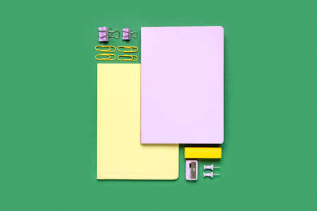 Notebooks with paper clips, sharpener and eraser on green background