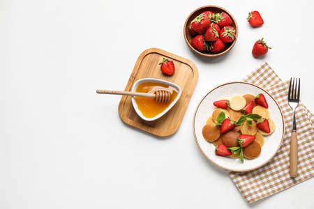 Plate with mini pancakes, delicious strawberry and honey on light backgroundの写真素材