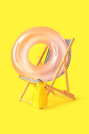 Wooden deck chair with inflatable ring and paddles on yellow backgroundの写真素材